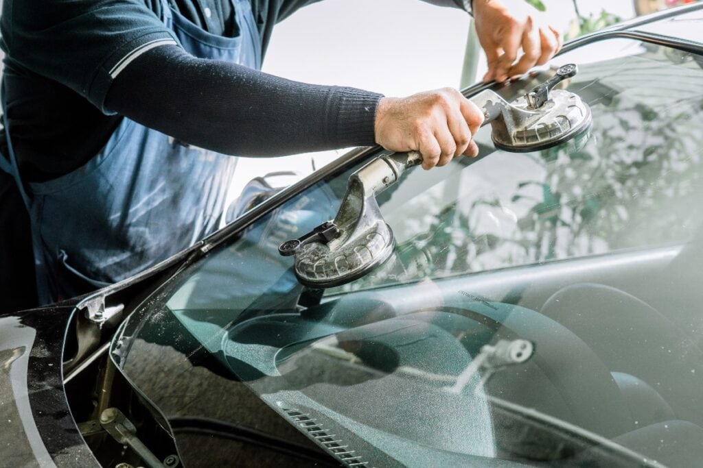 Mechanics man changing the broken windshield and automobile windshield or windscreen replacement of white car in Auto Repair Shop