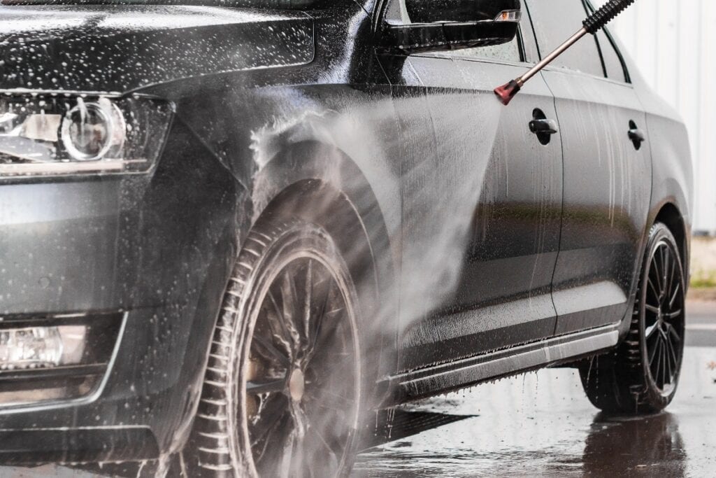 A man is washing a car at self service car wash. High pressure vehicle washer machine sprays foam.